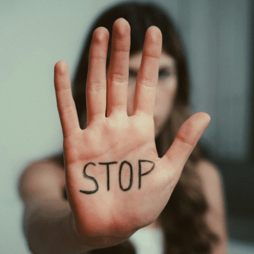 Femme de face tendant le bras pour montrer écrit sur la paume de sa main le mot : STOP